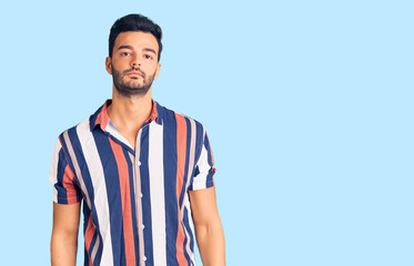 Young handsome hispanic man wearing casual  summer shirt with serious expression on face. simple and natural looking at the camera.