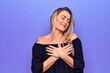 © Krakenimages.com - Young beautiful blonde woman wearing casual t-shirt standing over isolated purple background smiling with hands on chest, eyes closed with grateful gesture on face. Health concept.