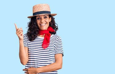 Wall Mural - Middle age beautiful woman wearing casual striped t shirt and summer hat smiling happy pointing with hand and finger to the side