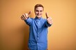 © Krakenimages.com - Young handsome redhead man wearing casual striped shirt over isolated yellow background approving doing positive gesture with hand, thumbs up smiling and happy for success. Winner gesture.