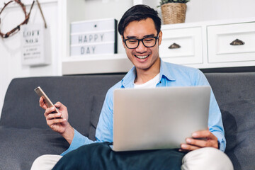 young smiling asian man relaxing using laptop computer working and video conference meeting at home.