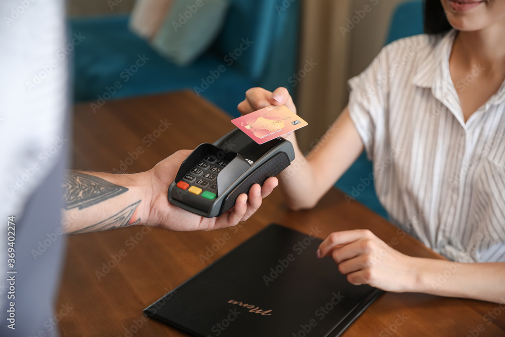 Woman paying bill in restaurant through terminal, closeup