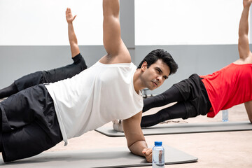 Wall Mural - Athletic Indian man doing side plank exercise outdoors on rooftop with friends