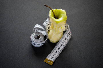 Eaten apple with measuring tape on black background. Fitness and diet concept