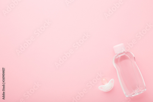 Transparent plastic bottle of oil and white soother for baby on light pink table background. Pastel color. Care about soft body skin. Closeup. Empty place for text or logo.