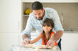 © Mangostar - Happy Latin girl and her dad rolling and kneading dough on kitchen table with flour powder. Father helping daughter to bake bread or pies. Parenthood concept
