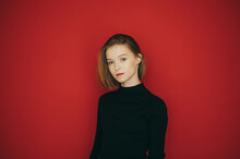 Stylish Lady In Dark Casual Clothes Isolated On Red. Beautiful Girl In A Black Sweater Stands In The Studio On A Red Background, Looks Into The Camera And Poses With A Serious Face. Isolated.