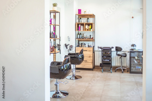 Empty black chairs and mirrors in barber shop. Interior of illuminated hair salon. Interior of modern hair salon. Empty interior of modern hairdressing salon