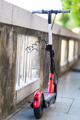 Red electric scooter parked and safely chained to a fence. Eco friendly green modern urban mobility concept of sharing transportation with electric scooters for rent in Ljubljana, Slovenia.