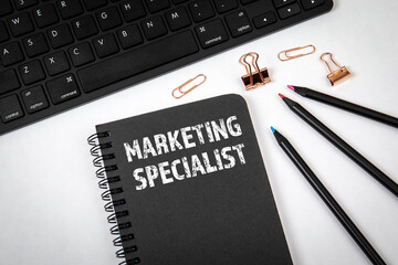 Canvas Print - MARKETING SPECIALIST. Notebook, black keyboard and office supplies