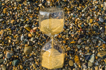 Hourglass on sea pebbles on the ocean coast.