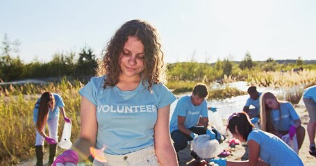 Poster - Group of volunteers collecting garbage, trash outdoor in wildlife. A beautiful young Caucasian girl holding a trash bag and looking, smiling at camera. Conservation movement environmentalism concept.