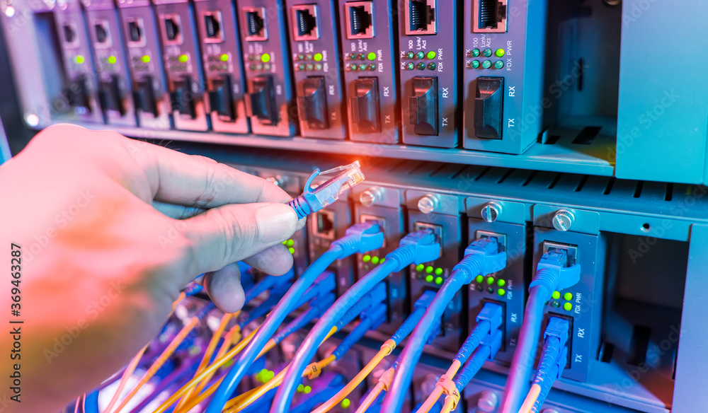 man working in network server room with fiber optic hub for digital communications and internet - obrazy, fototapety, plakaty 