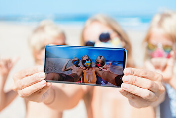 Funny kids with mother taking selfie photo by smartphone on tropical sea beach. Rule to wear face covering mask at public places due coronavirus COVID 19. Family holidays with children, summer travel.