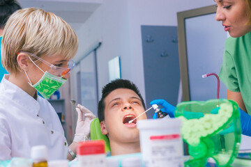 Wall Mural - Closeup picture of a female dentist examining teenage boy's teeth in the dental office.