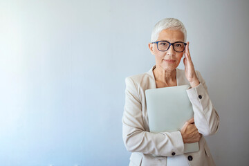 Studio portrait of a confident mature woman posing against a gray background with laptop. Senior business woman standing against grey background with copy space. 