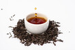 loose black tea next to a cup of tea on a white background