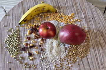 Poster - High angle shot of an apple, a mango, a banana, and different cereals on a round wooden table