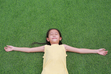 Close eyes little Asian child girl with two ponytail hair lying on green grass in the garden.