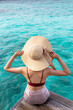 © Avirut S. - Girl on the wooden jetty looking to the ocean. Beautiful woman on wooden pier by the sea outdoors holding her hat. Back view of a young girl sitting on a pier with sea and sky in background.