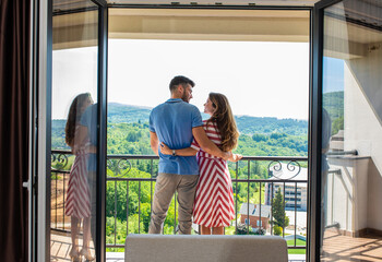 Wall Mural - rear view of smiling couple in the hotel room standing at terrace embracing each other.