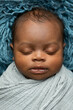 © Ursula Page - Close-up sleepy swaddled African-American newborn baby boy laying on a blue rug in a basket with copy space