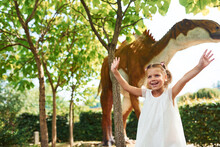 Cheerful Little Girl Having Fun In Park With Dinosaur Replicas Outdoors