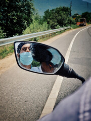 Closeup shot of two men riding a motorbike while wearing masks on a sunny day