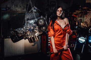 Brave and very sexy looking young woman posing with a big wrench, surrounded by motorcycle details and with a motorbike on the background