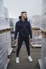 Wall Mural - Vertical shot of a cool young man wearing a hoodie and sweatpants standing near new furniture