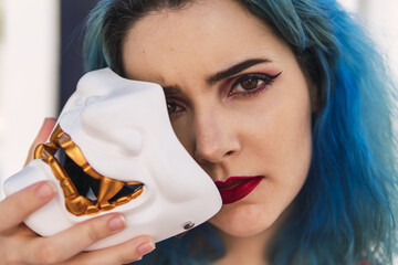 Wall Mural - Closeup shot of a cool young lady with blue hair holding a mask in her hand