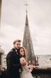 © Andriy Medvediuk - Happy newlywed. beautiful bride and stylish groom are hugging on the balcony of old gothic cathedral with panoramic city views