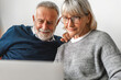© Art_Photo - Senior couple family having good time using laptop computer together.Happy elderly husband and wife checking social media and reading news or shopping online while sitting on sofa at home