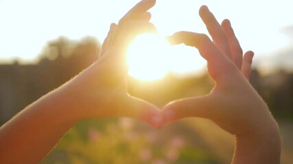 The sun shines through the hands arranged in a heart shape