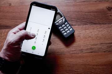 Wall Mural - Top view of a smartphone held by a person's hand with an old cellphone model on the background