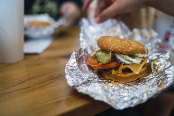 Poster - Selective focus shot of cheeseburger in a foil on a table