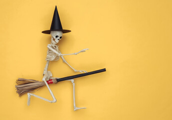 Skeleton in a witch's hat on a broomstick. Yellow background. Halloween minimalistic concept. Top view. Flat lay