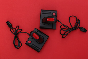 Canvas Print - Two wired retro joysticks with wound cable on red background. Video game, gaming. Top view