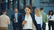 © Fractal Pictures - Appealing young caucasian businesswoman with smartphone walks in corporate neighbourhood outdoors. Business people lifestyle. Social distancin Technology.