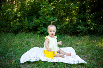 portrait of a little girl on a blanket with a yellow watering can in nature