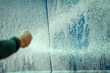 Wall Mural - Close-up worker spray white foam to clean car. Blue car wash with white soap foam. Auto care business. Car cleaning and shining before waxing service. Vehicle cleaning service. Manual car wash.