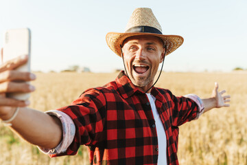 Wall Mural - Image of excited adult man taking selfie on cellphone at cereal field