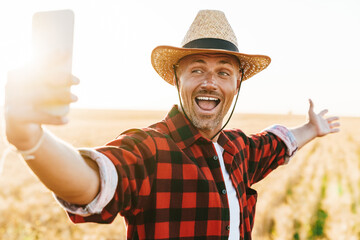 Wall Mural - Image of excited adult man taking selfie on cellphone at cereal field