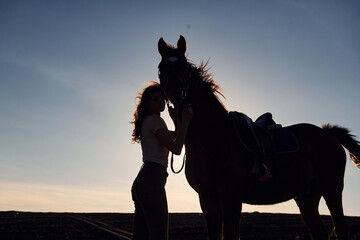 Young woman standing with her horse in agriculture field at sunny daytime