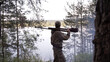 © spocktv - View from back of hunter in camouflage puts hunting rifle on his shoulder and looks at river from forest. Outdoor activity concept. Summer hiking in wilderness area.