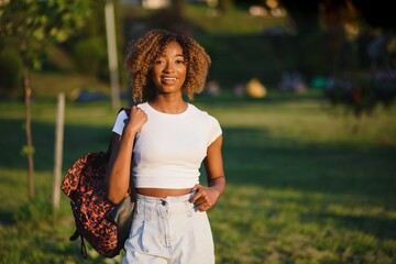 Portrait of beautiful african american woman smiling and looking away at park during sunset. Outdoor portrait of a smiling black girl. Happy cheerful girl laughing at park with colored hair band.