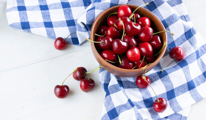 Fresh cherries in a clay bowl on the white table and a kitchen counter in a blue cage. Top view