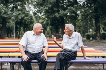 two old senior adult men have a conversation outdoors in the city park.