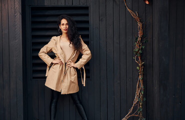 Woman with black curly hair standing against black wooden building exterior