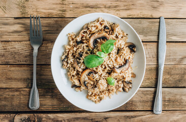 Wall Mural - Traditional Italian mushroom risotto on rustic wooden background. Classic Risotto with mushrooms served on a white plate. Top view with copy space